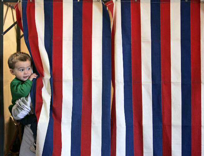 Criança espia pela cortina da cabine enquanto sua mãe vota em Wisconsin