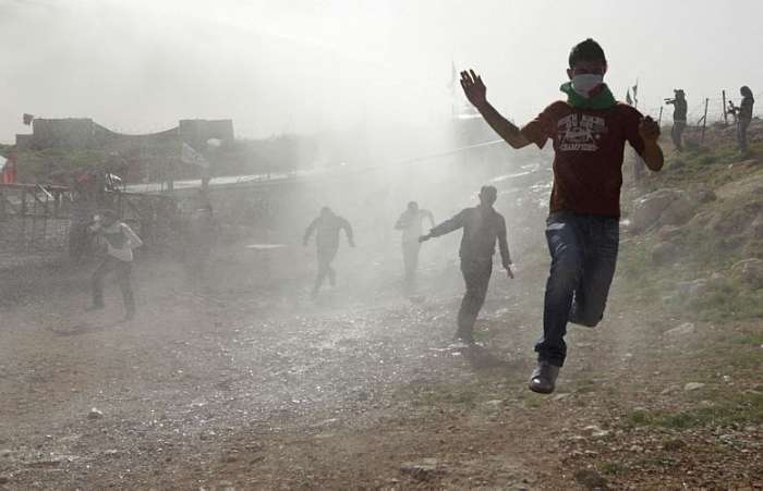 Protestantes palestinos e estrangeiros correm da polícia após protesto conta a barreira no West Bank
