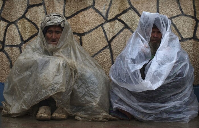 Afegãos se protegem de chuva e frio na cidade de Mazar-e-Sharif, ao norte de Cabul