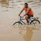 Homem atravessa de bicicleta área inundada na Ceagesp, zona oeste da Capital
