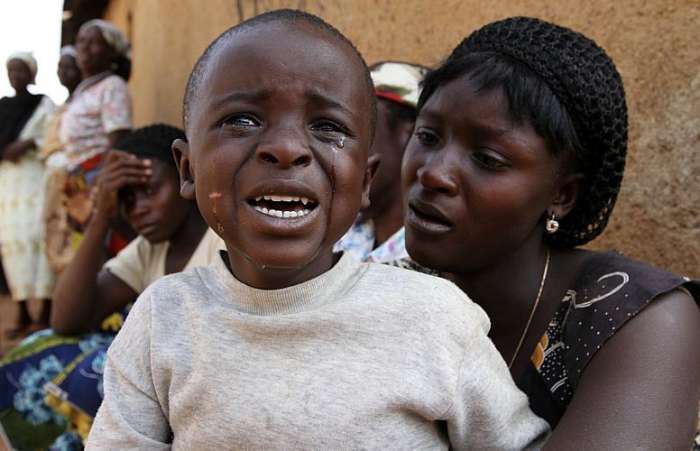 Menino sentado ao lado de sua mãe chora durante funeral dos mortos por questões religiosas, Nigéria