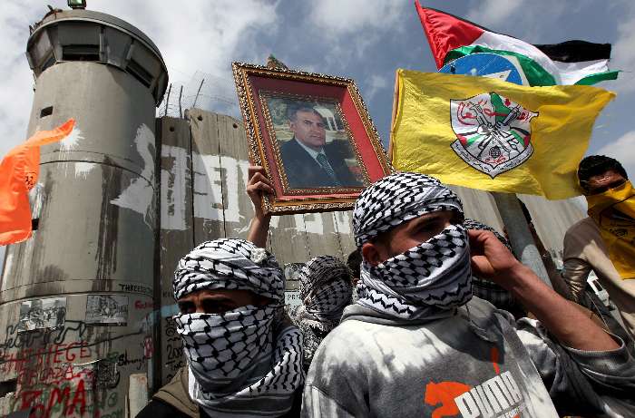 Jóvens seguram retrato do líder de Fatah durante marcha contra restrições aos palestinos