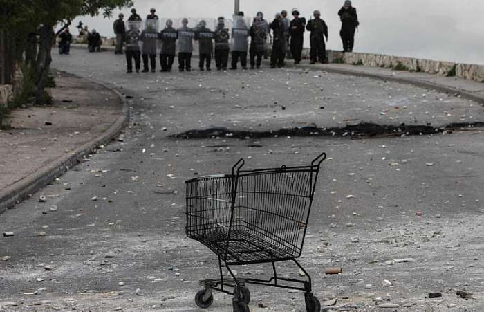 Carrinho de supermercado queimado é colocado em frente a bloqueio de soldados
