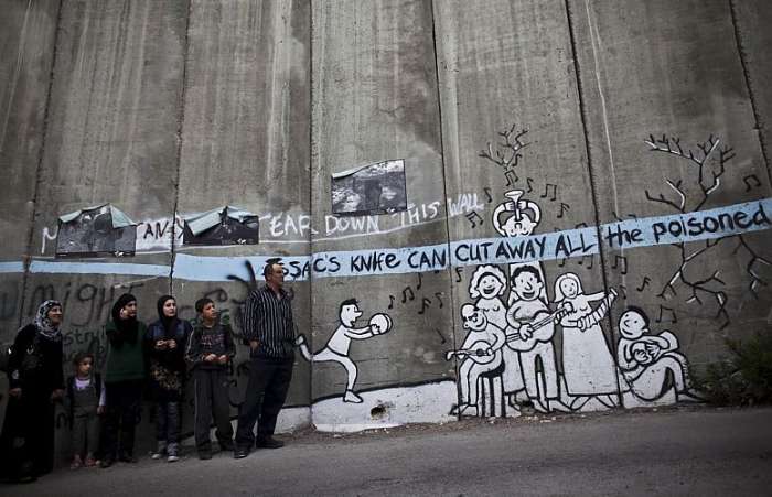 Palestinos esperam caminhão ao lado do muro separatista em West Bank, cidade de Bethlehem