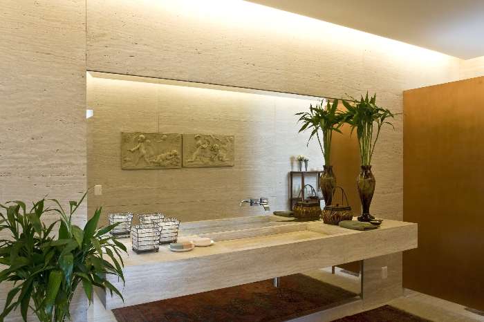 Lavabo é todo revestido de mármore travertino bruto; a divisória que esconde o vaso é de cobre