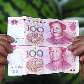Vendedor de melancia observa as notas de 100 Yuan, em mercado de Changzhi, na China Vendedor de melancia observa as notas de 100 Yuan, em mercado de Changzhi, na China