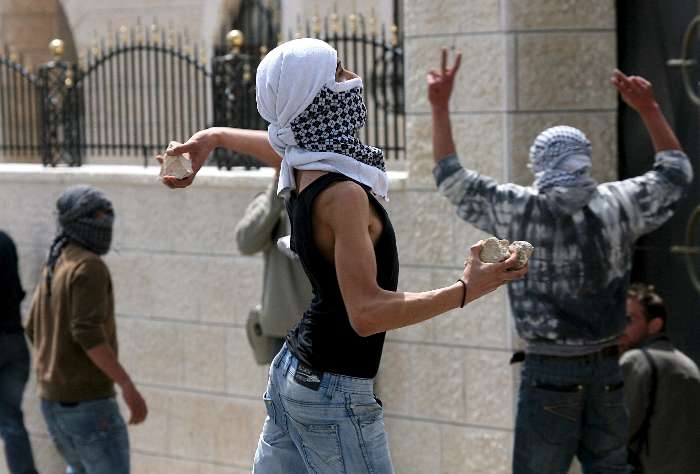 Jovem palestino joga pedra contra a torre militar israelita construída para separar Israel