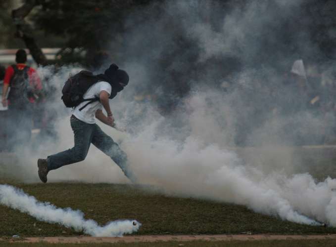 Manifestante tenta se proteger do ataque da PM durante confronto na USP