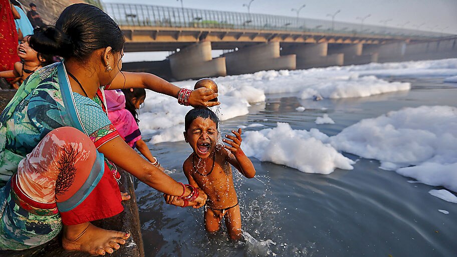 Anindito Mukherjee / Reuters - Indiana banha o filho nas águas poluídas do rio Yamuna em Nova Délhi, na Índia. Foto: Anindito Mukherjee / Reuters