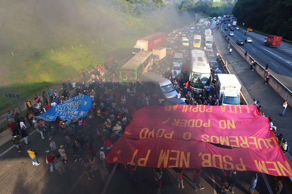 &nbsp;Cerca de&nbsp;100 pessoas interditam todas as faixas da rodovia. Os manifestantes estenderam bandeiras da liderança dos movimentos&nbsp;e queimaram pneus