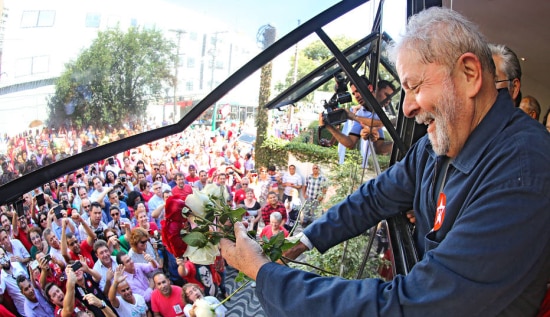 O ex-presidente Luiz Inácio Lula da Silva aparece na janela enquanto partidários do PT realizam um abraço coletivo no prédio do Instituto Lula, na , zona sul da capital
