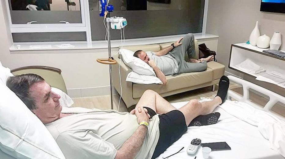 Jair Bolsonaro e o filho Carlos assistem à TV no quarto