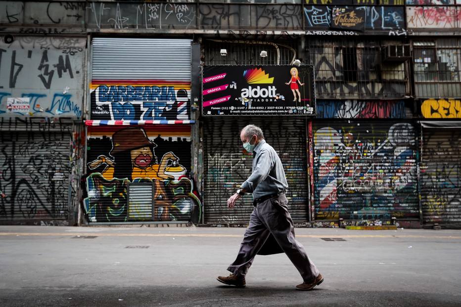 Um homem caminha na frente de estabelecimentos comerciais fechados na capital paulista.