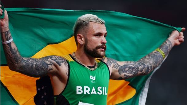 Vinícius Rodrigues mostra bandeira do Brasil após conquistar o ouro na prova dos 100m rasos da classe T63