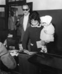 Mulher, segurando um bebê no colo, deposita seu voto na urna durante votaçõo das eleições presidenciais de 1960, São Paulo, SP, 04/10/1960. 