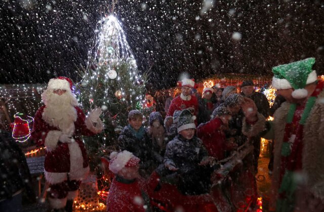 Yves Herman/Reuters Serge Hennebel e um homem vestido de Papai Noel interagem com crianças que visitam o jardim transformado em vila natalina.