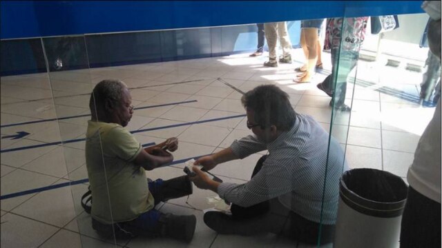 Facebook.com/isabel.paiva.5076 O gerente de uma agência da Caixa Econômica Federal sentou-se no chão para atender um cliente.
