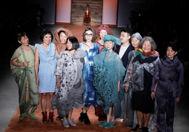 Nacho Doce/REUTERS A estlista Fernanda Yamamoto, à esquerda, de vestido azul listrado, com sua equipe e integrantes da comunidade Yuba, que coloca o coletivo sobre interesses individuais
