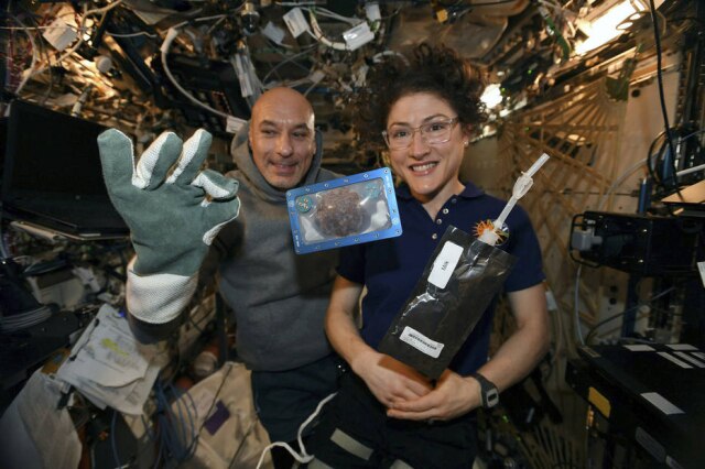 Nasa via AP A astronauta Christina Koch e o astronauta italiano Luca Parmitano com um dos cookies assados na Estação Espacial Internacional.