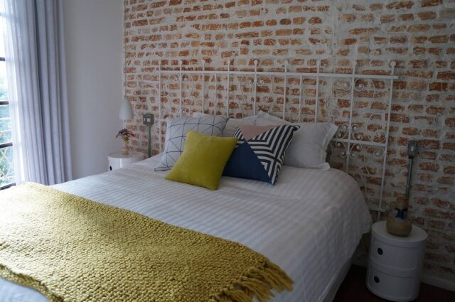 Divulgação A arquiteta Helena Kallas, do Mandril Arquitetura, usou uma grade de metal antiga para fazer a cabeceira deste quarto. A peça está parafusada na parede de tijolos aparentes