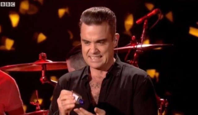 Reprodução/YouTube Robbie Williams faz expressão de 'nojo' e higieniza mãos com álcool após tocar em fãs em show.