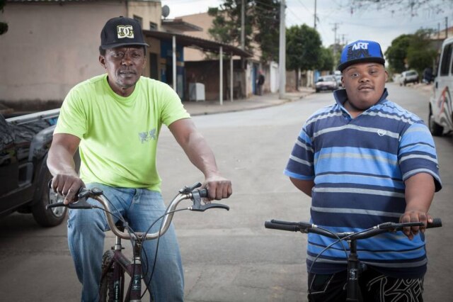Ricardo Lima / Fundação Síndrome de Down Alexsander Marcílio pousa ao lado do pai, Wagner, enquanto andam de bicicleta. Família acredita que a representatividade das pessoas negras com Down é utópica diante do que veem nos dias de hoje.