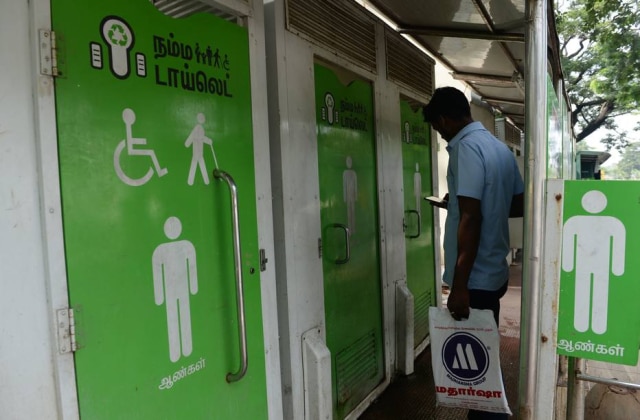 Arun Sankar / AFP Indiano olha o celular enquanto aguarda para usar banheiro público em Chennai, na Índia. Instalação foi feita pelo governo indiano para evitar que pessoas defequem em lugares impróprios. Imagem de novembro de 2017.