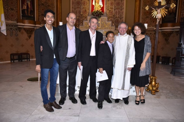 David Harrad/Arquivo Pessoal O casal Toni Reis e David Harrad e seus filhos Allinson (esquerda), Felipe (centro) e Jéssica (direita), ao lado do padre Helio, em batizado no domingo, 23 de abril.