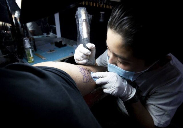 Juan Carlos Sanchez/AFP Brandon Burgos, de 11 anos, tatua uma pessoa no estúdio do pai, na cidade de Puebla, no México.